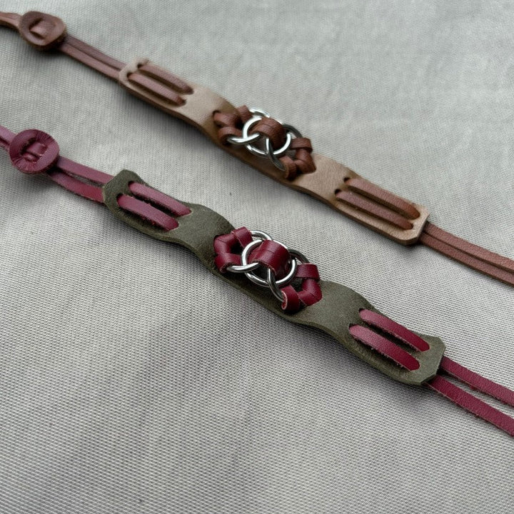 Two handmade leather bracelets with metal ring accents on neutral fabric background