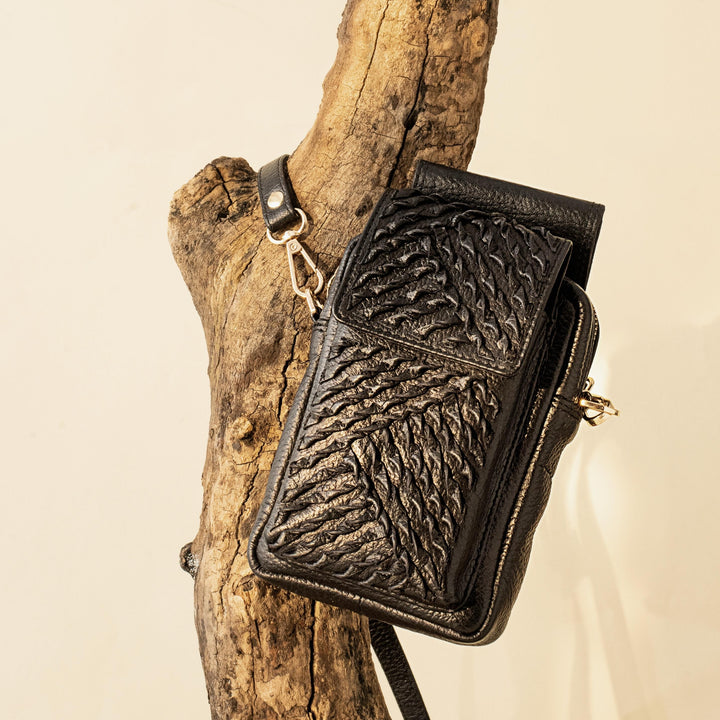 Black leather textured crossbody bag hanging on rustic wooden branch background