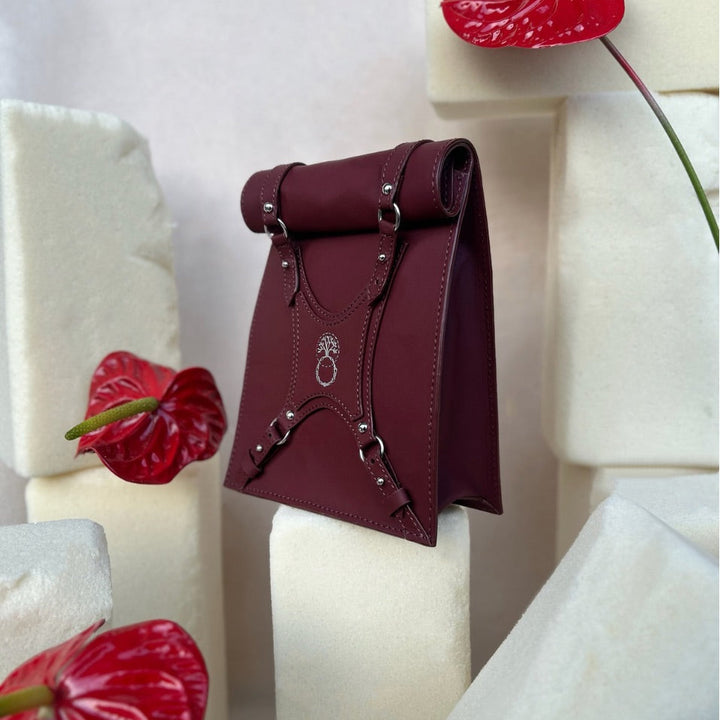 Maroon leather handbag with silver buckles displayed on white foam blocks with red anthurium flowers