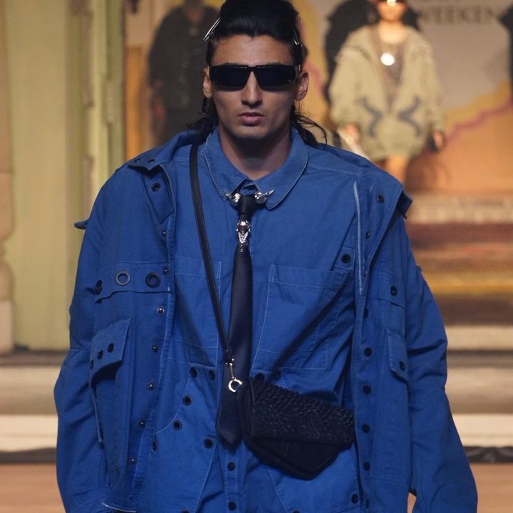 Male model in blue layered jacket and shirt with black tie and sunglasses on runway