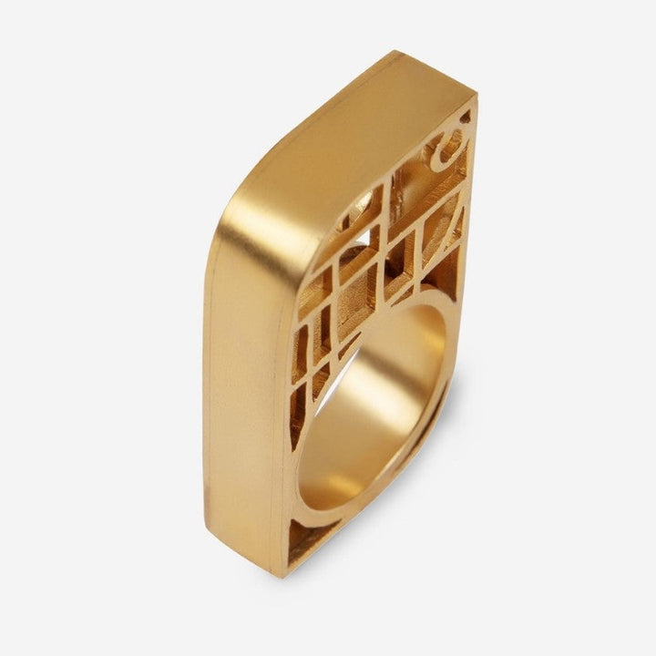 Gold-toned metal ring with a square top featuring a cutout geometric pattern on a white background