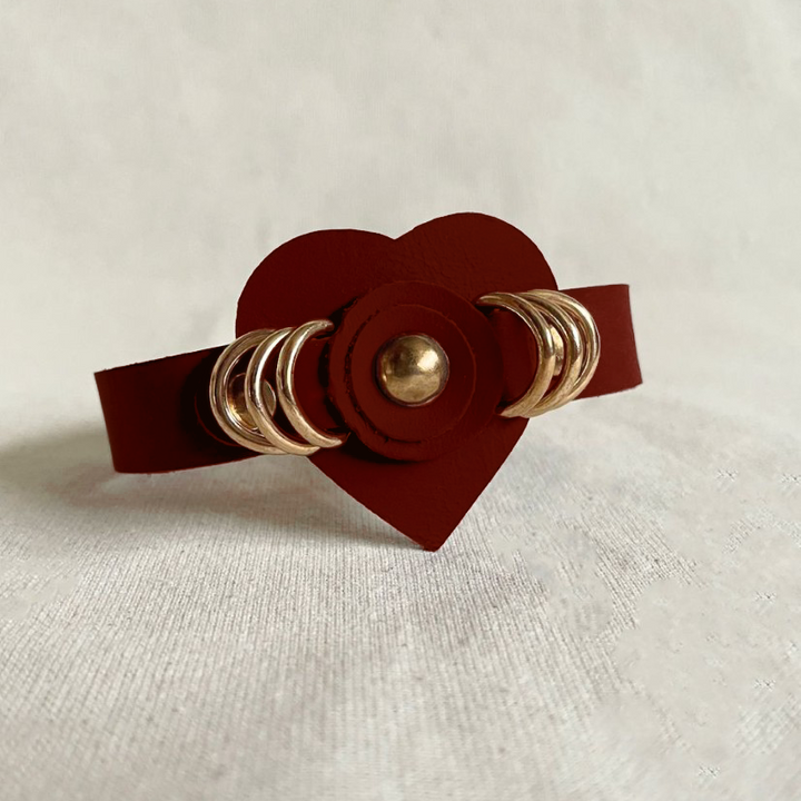 Timeless tan leather cuff bracelet with heart centerpiece and gold rings on white fabric