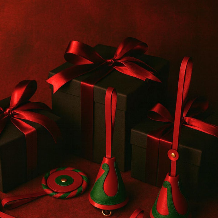 Black gift boxes wrapped with red satin ribbons surrounded by red and green leather Christmas ornaments