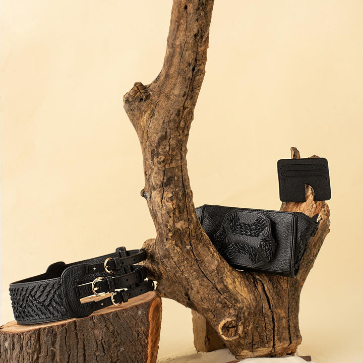 Black leather belt, wallet, and cardholder displayed on rustic wood pieces against a beige background