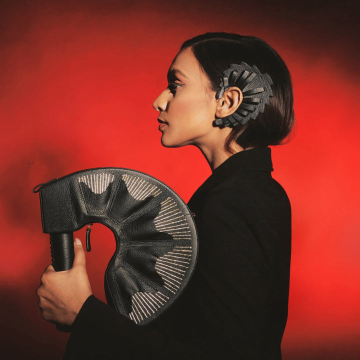 Profile of woman in black holding black leather curved bag, black headpiece, red background