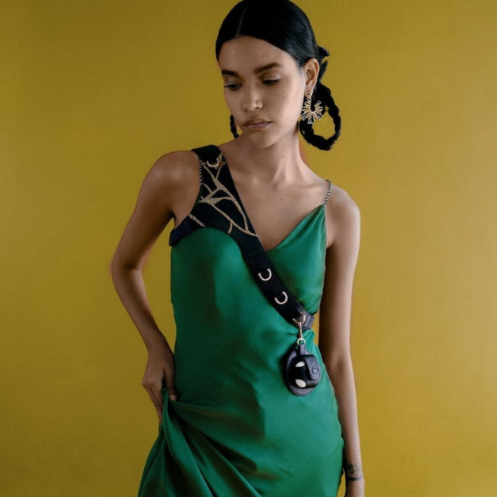 Woman in green satin dress with black strap and artistic gold earrings against yellow background