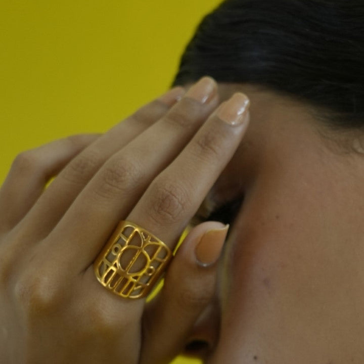 Close-up of hand with a gold geometric metal ring on finger against yellow background