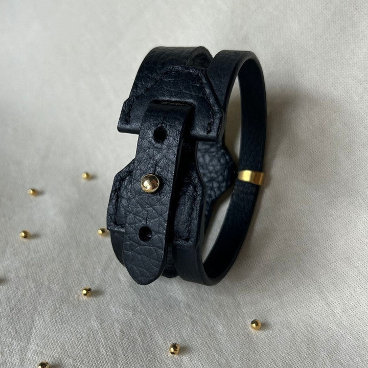 Handcrafted black leather upcycled bracelet with gold accent on beige fabric, small gold beads scattered