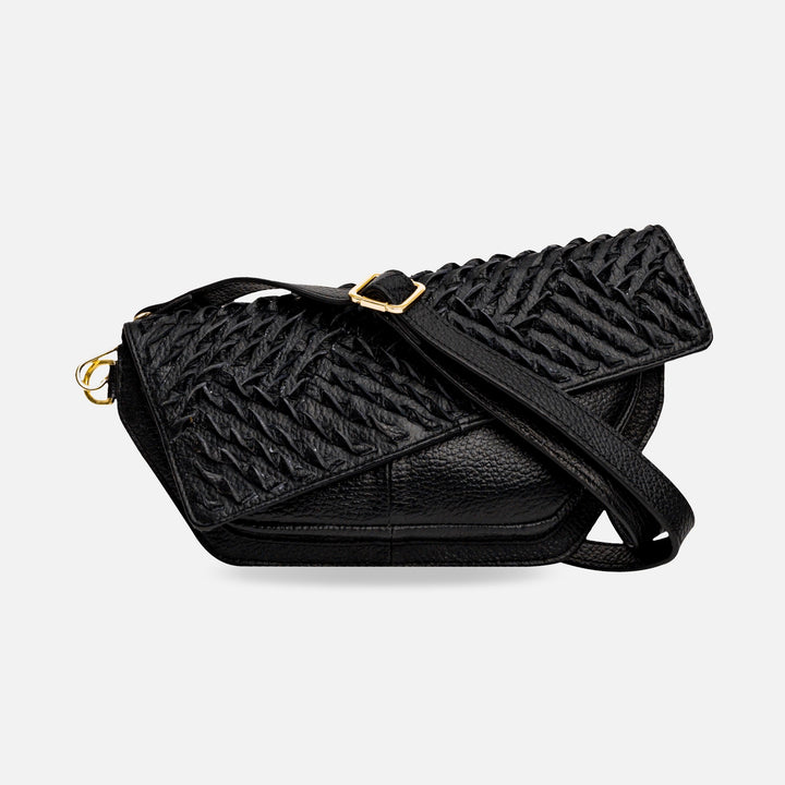 Black textured leather crossbody bag with braided flap and gold buckle strap on white background