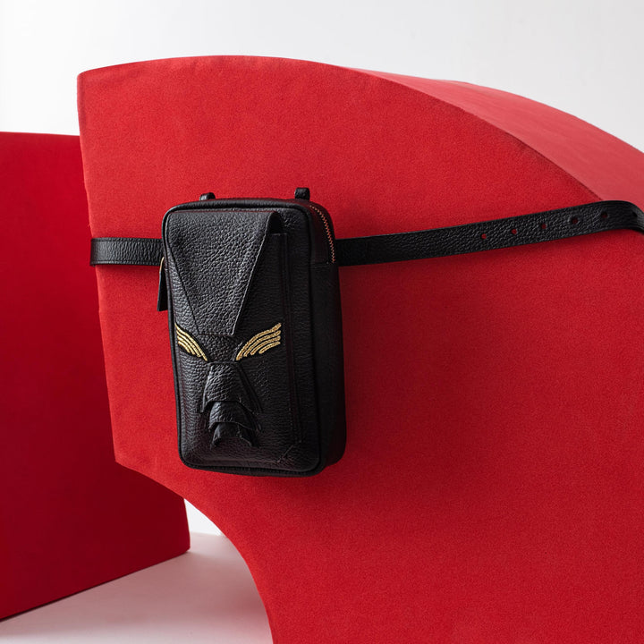 Black leather belt bag with gold wing design on red abstract curved backdrop