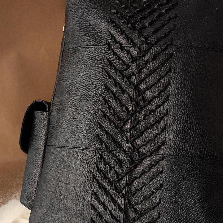 Black leather bag with textured herringbone pattern on front against brown and white background