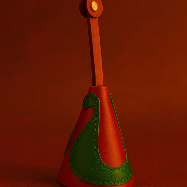 Red and green leather bag charm with gold button on red background