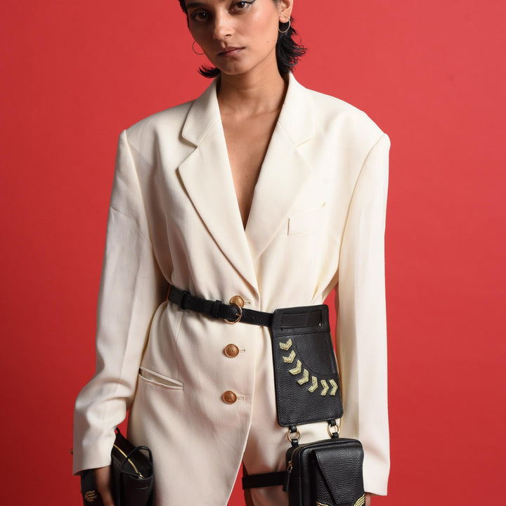Model wearing oversized white blazer with gold buttons and black leather belt bags against red background