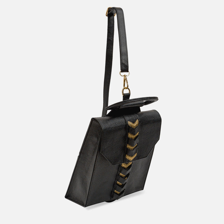 Black leather crossbody bag with gold chevron detailing and adjustable strap on white background
