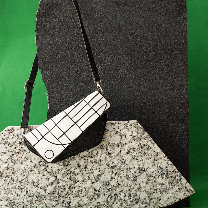 Black and white geometric patterned handbag with black strap on textured stone slabs against green background