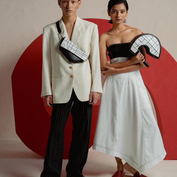 Fashion models in modern black and white outfits with geometric bags posing against red abstract background