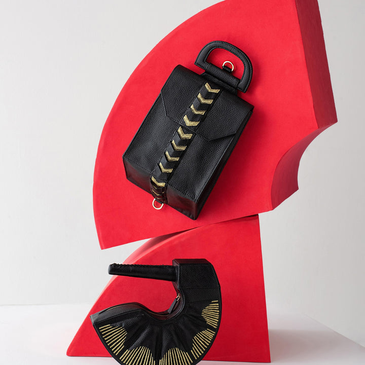 Two black textured handbags with gold accents displayed on a bold red sculptural stand