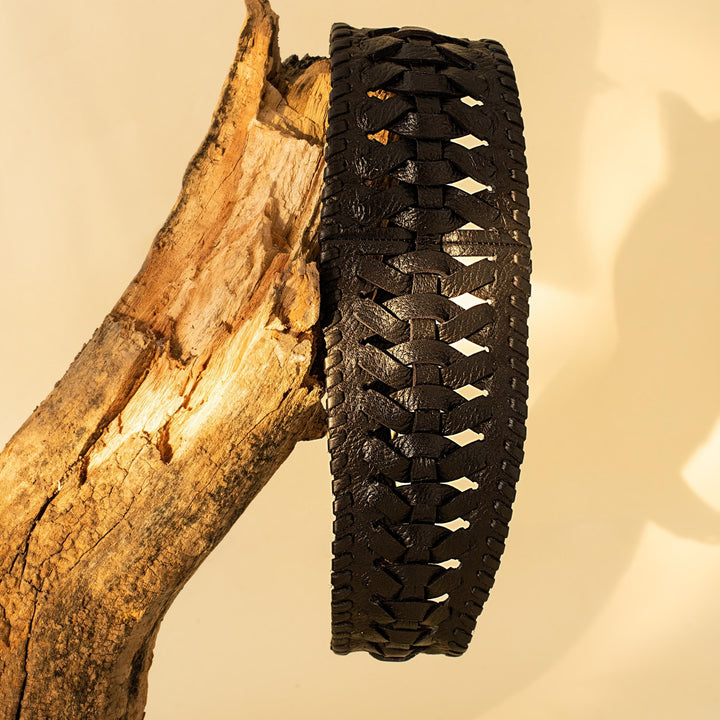 Black woven leather bracelet displayed on a textured tree branch against beige background