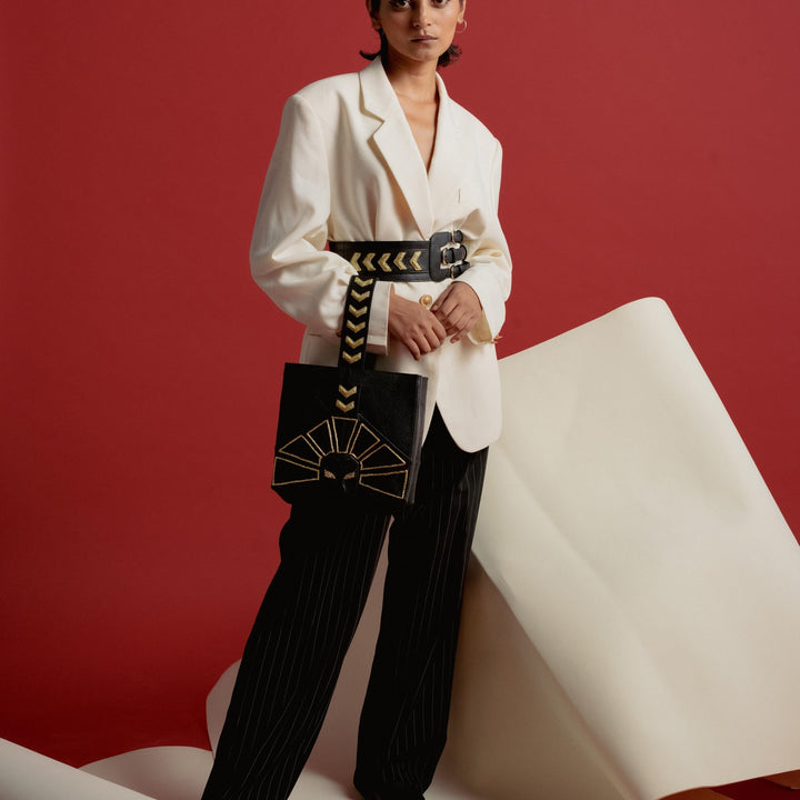 Woman in oversized white blazer and black pinstripe pants holding black bag with gold design on red background