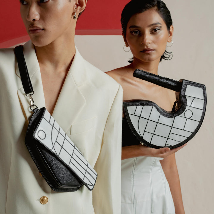 Two models showcasing black and white geometric handbags with leather details against abstract red and beige backdrop