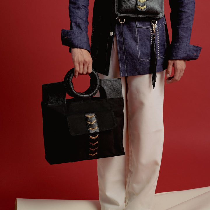 Person in denim jacket and cream pants holding black handbag with circular handle and waist bag on red background