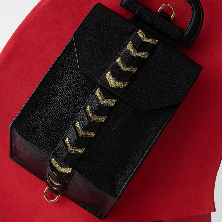 Black textured leather handbag with gold chevron strap on curved red surface