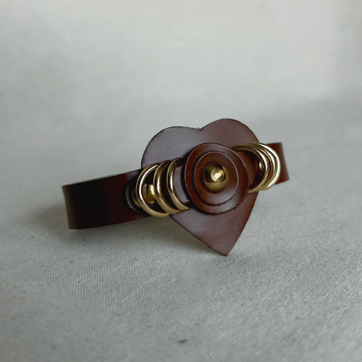 Timeless chocolate vegan leather cuff bracelet with gold rings and heart centerpiece on neutral fabric
