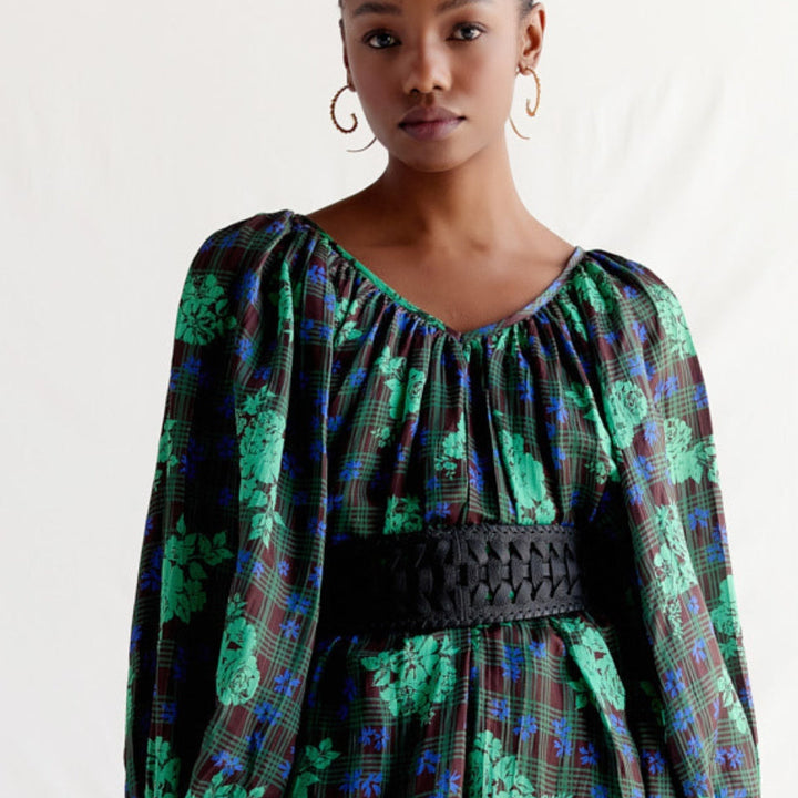 Woman wearing green floral and plaid dress with puffed sleeves and black woven belt