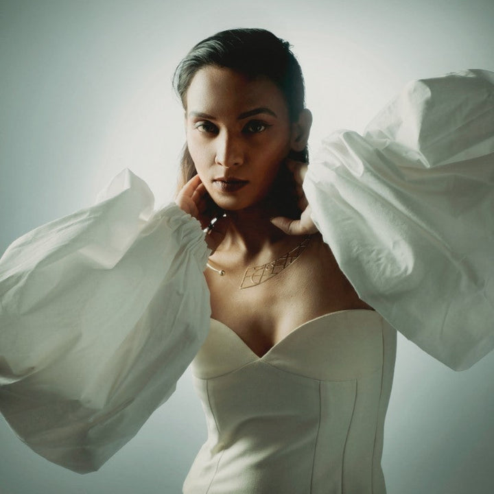 Woman wearing white corset top with large puffed sleeves and geometric gold necklace