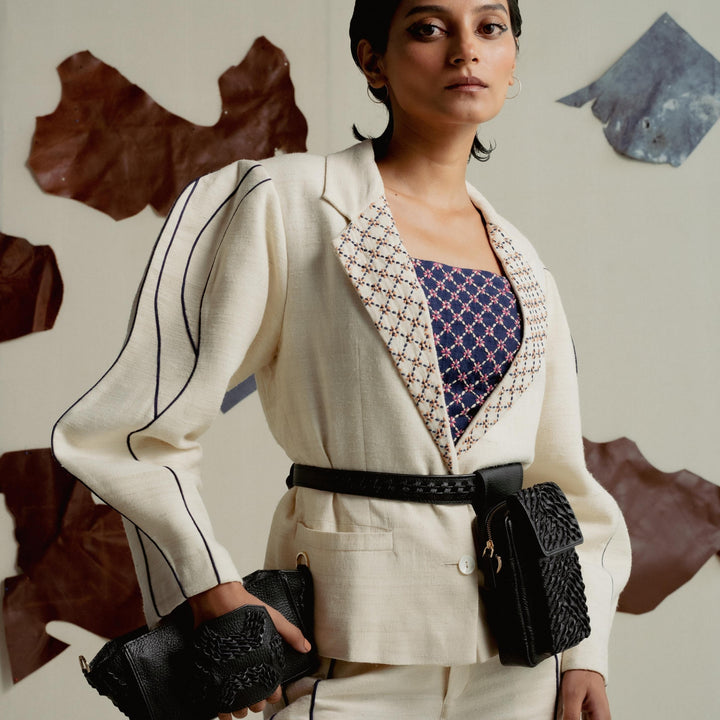 Woman wearing cream pantsuit with black striped sleeves, patterned navy top, black belt bag, and matching clutch