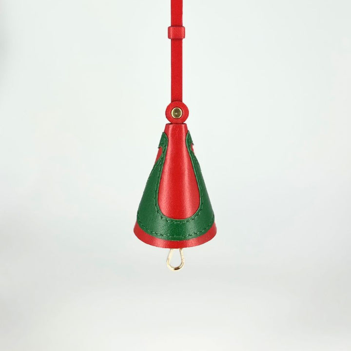 Red and green leather handbag charm with gold hardware hanging against white background