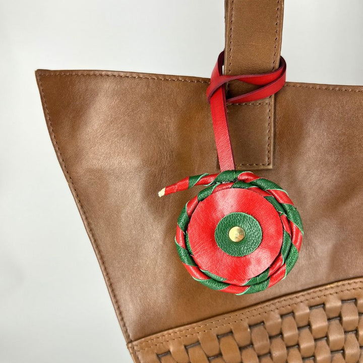 Brown leather tote bag with woven detail and red-green braided leather charm attached