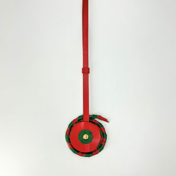 Red leather tag with circular charm featuring green and gold accents on white background