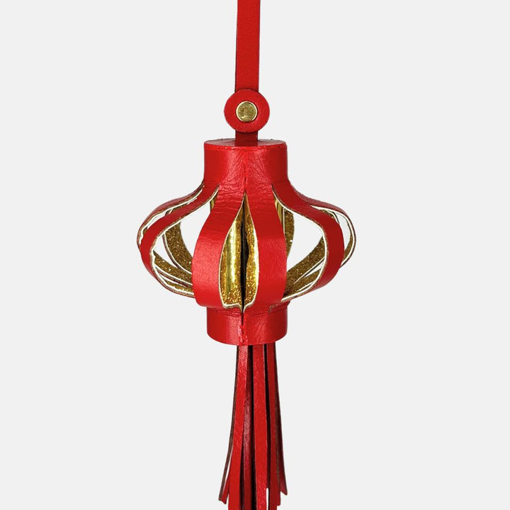 Red and gold hanging lantern charm ornament with tassels on white background