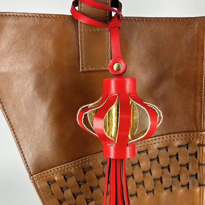 Red leather lantern charm with gold accents hanging on brown woven leather bag