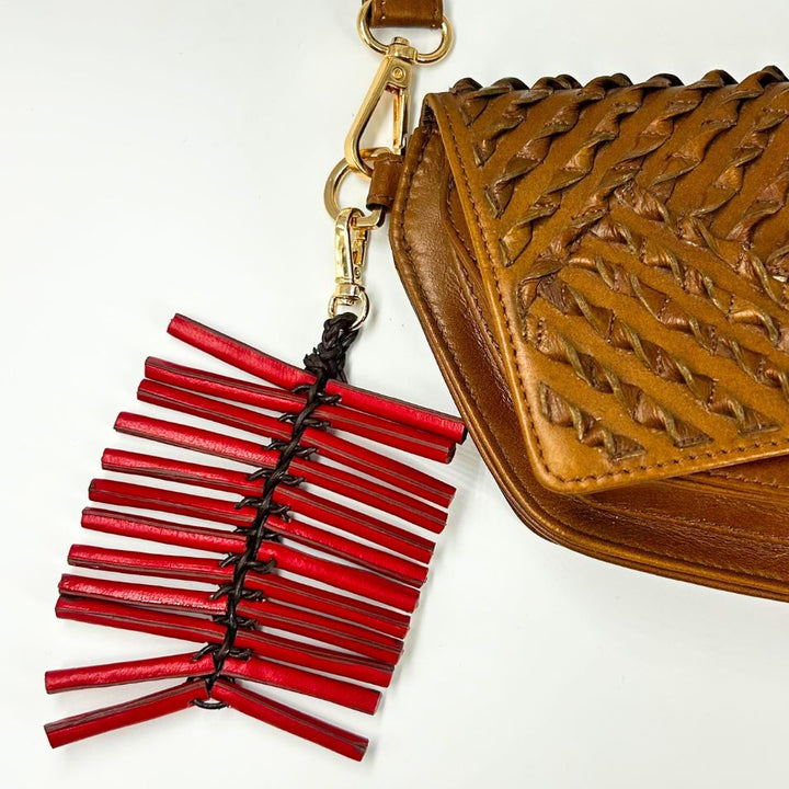 Brown woven leather handbag with attached red leather tassel keychain on white background