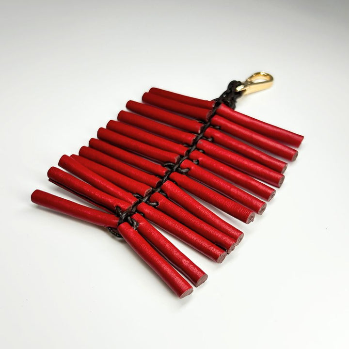 Red wooden stick keychain with black braided cord and gold clasp on white background