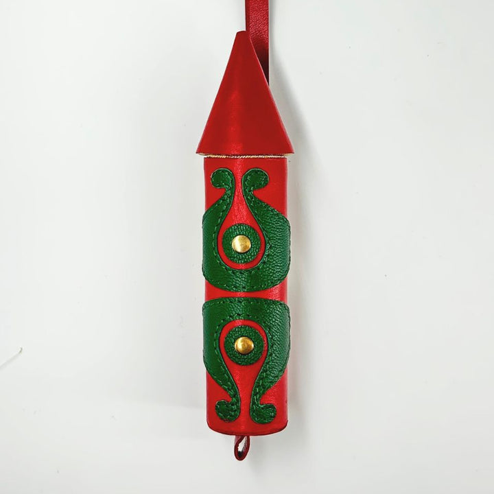 Red rocket-shaped leather charm with green embossed decorative patterns and gold studs on white background