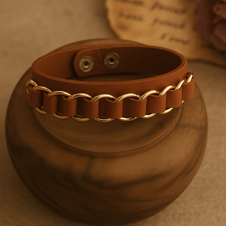 Brown leather bracelet with gold chain detail on wooden round stand against beige background