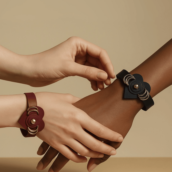 Two hands wearing leather flower bracelets, one in black and one in dark red, on a beige background