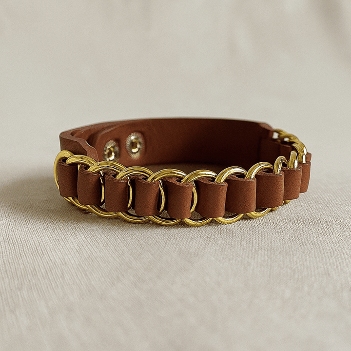 Brown leather bracelet with gold chain links on beige fabric background